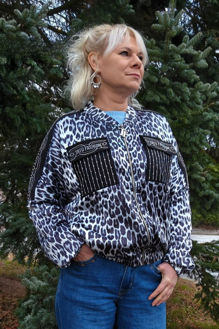 Nainen leopardikuosisessa satiinitakissa, jossa kimaltavat rintataskut, seisoo puiden edessä.